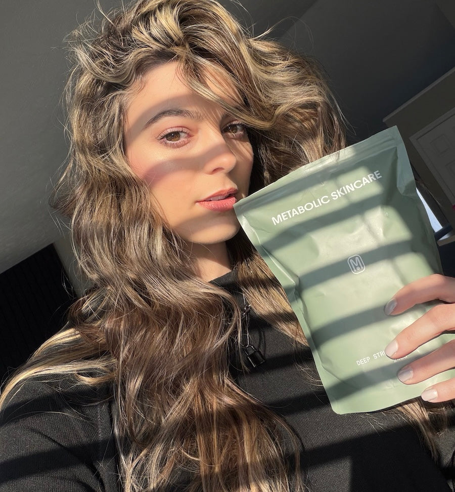 Woman holding a Metabolic Skincare product package with sunlight filtering through her hair.