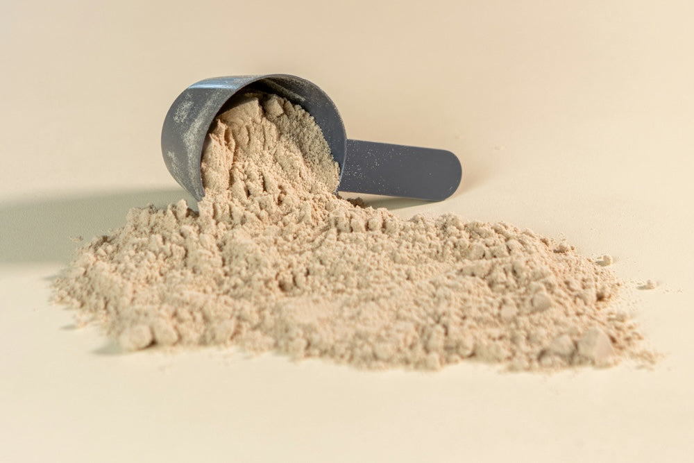 Scoop of a powdered supplement dumped out onto a cream colored surface