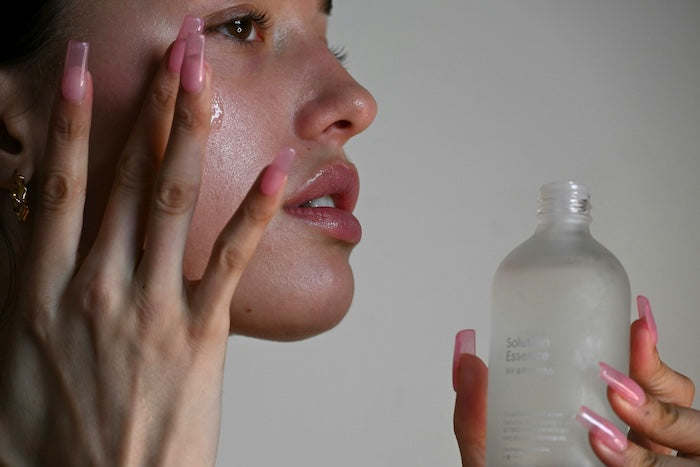 Woman applying a clear bottle product to her face against a neutral background